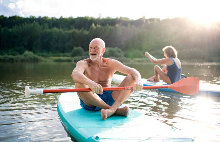 Senior couple paddleboarding on lake in summer